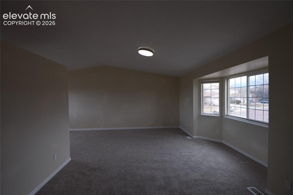 Image 8 of 44: Spacious room featuring carpeting, neutral wall tones, a vaulted ceiling, a