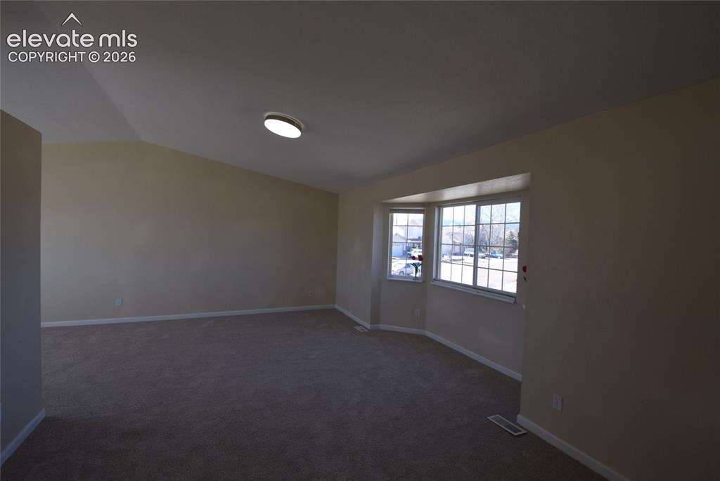 Image 9 of 44: Spacious room featuring a bay window, neutral wall paint, and gray carpet f