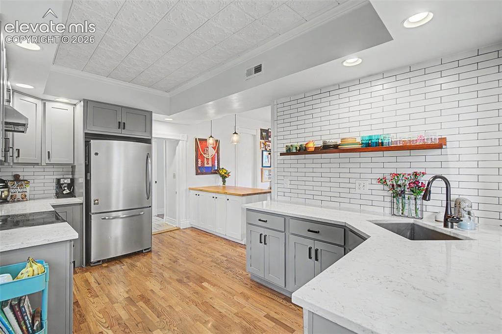 Image 25 of 50: Updated kitchen featuring light gray cabinetry, white tile backsplash, stai
