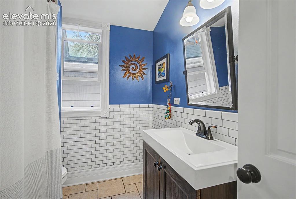 Image 32 of 50: 3/4 Bathroom on main level featuring white tiling, a dark wood-finish vanit