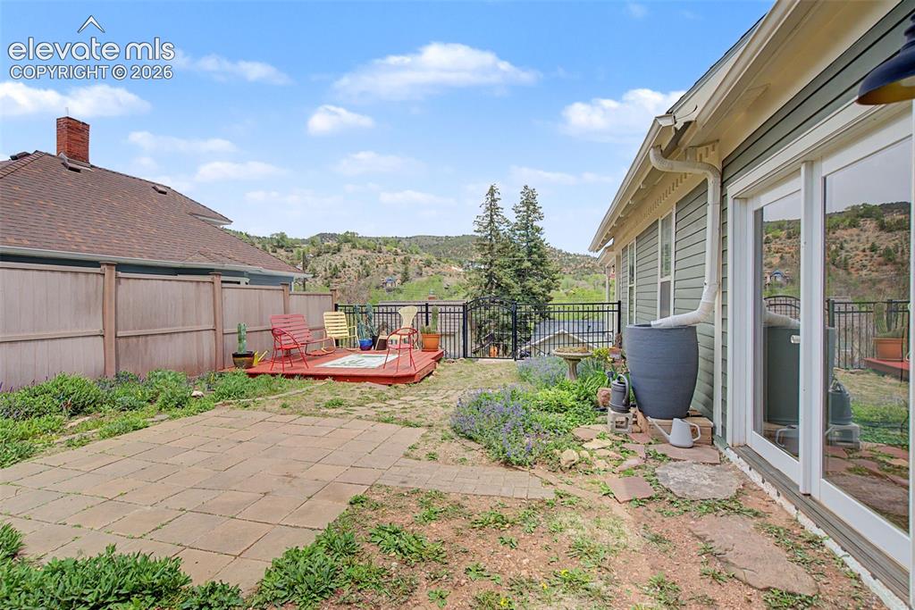 Image 44 of 50: Outdoor living area featuring a wooden deck, a stone patio, and fencing