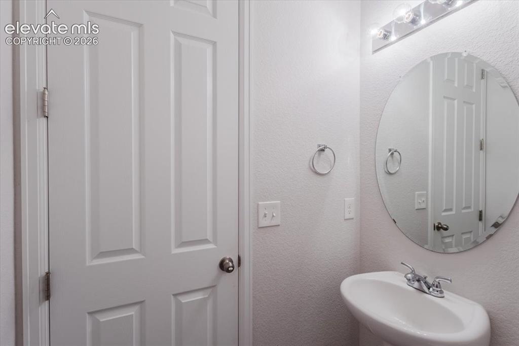 Image 13 of 50: Pedestal sink with chrome faucet, circular frameless mirror, and a five-lig