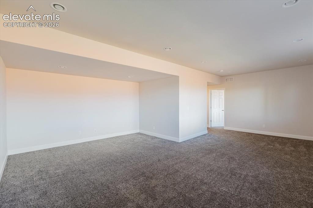 Image 21 of 50: Spacious room featuring neutral carpeting, white baseboards, and recessed c