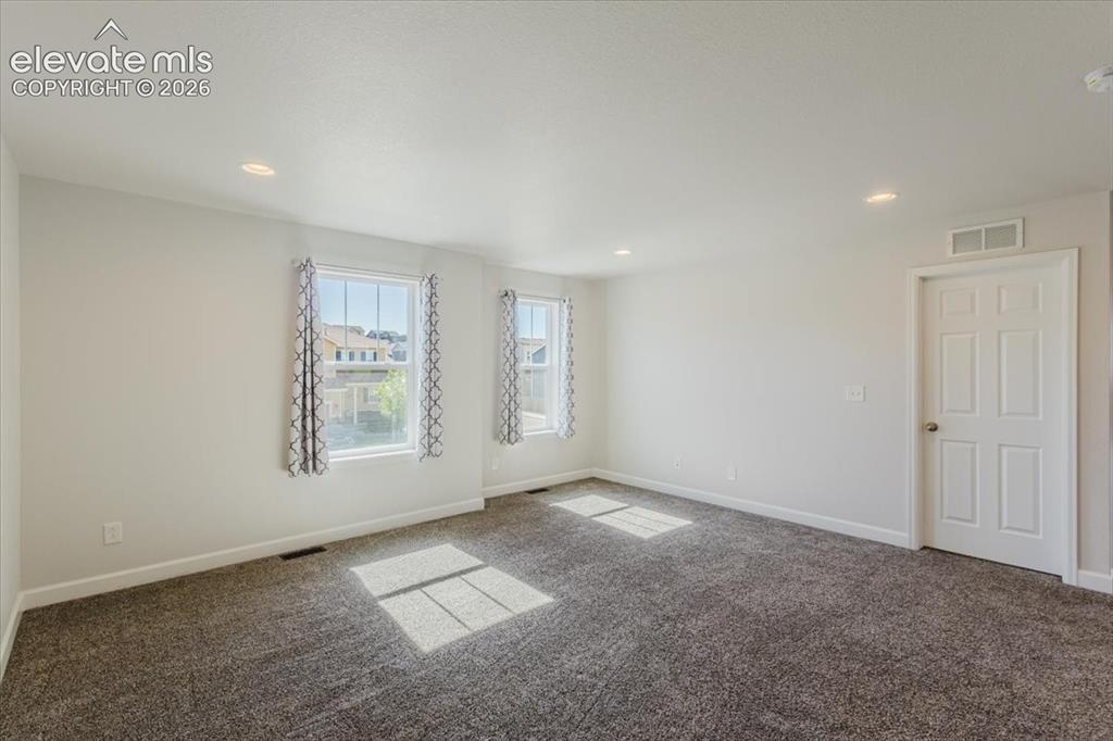 Image 34 of 50: Spacious room featuring neutral carpeting, two windows, recessed lighting, 
