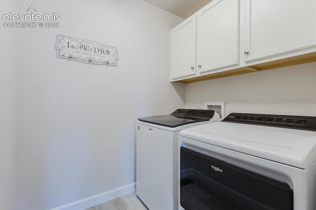 Image 37 of 50: Laundry area featuring light-toned wood-finish flooring, white wall cabinet
