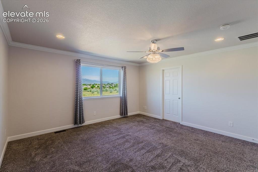 Image 40 of 50: Carpeted room featuring a large window, crown molding, a ceiling fan with i