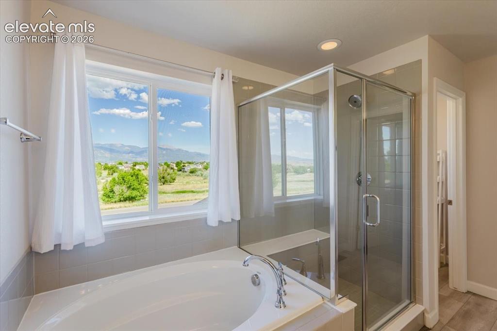 Image 42 of 50: Soaking tub with chrome fixtures, framed by a large window with white curta