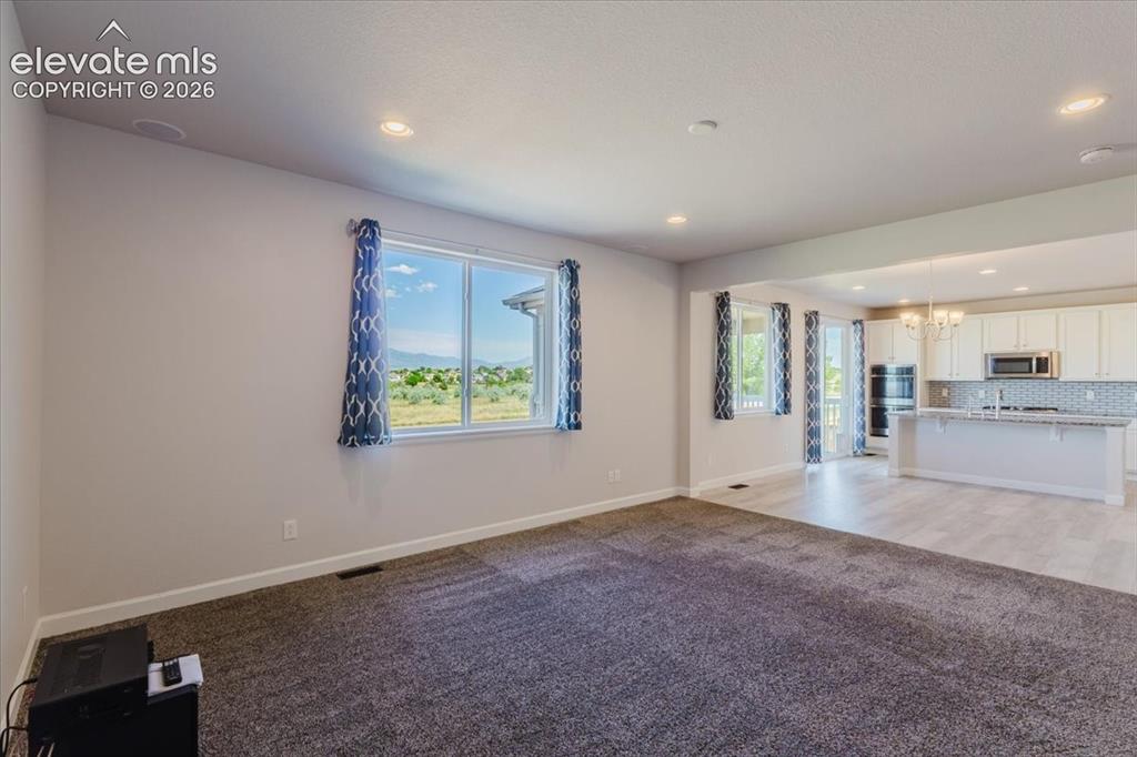 Image 50 of 50: Spacious open-concept living area featuring soft gray carpeting and recesse