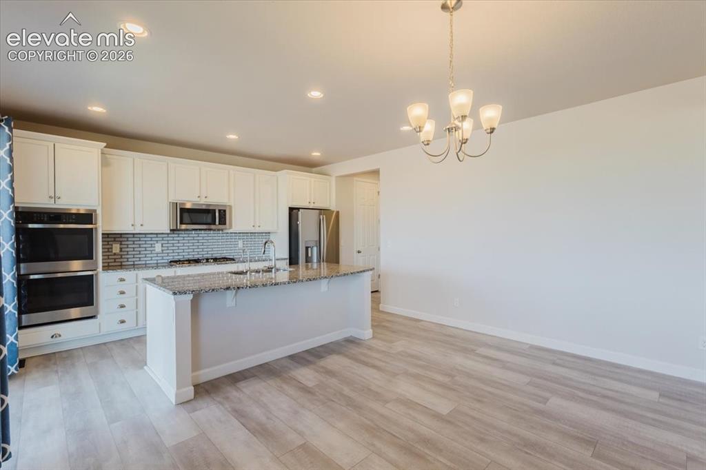 Image 7 of 50: Kitchen featuring white cabinetry, stainless steel appliances, a tiled back