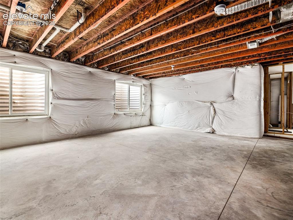 Image 21 of 24: Unfinished basement with exposed ceiling joists, concrete flooring, two win