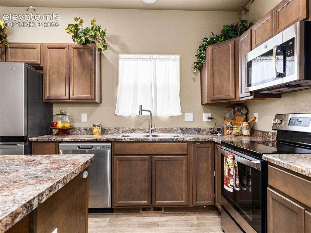 Image 9 of 24: Hardwood-style flooring, stainless steel appliances, brown wood-finish cabi