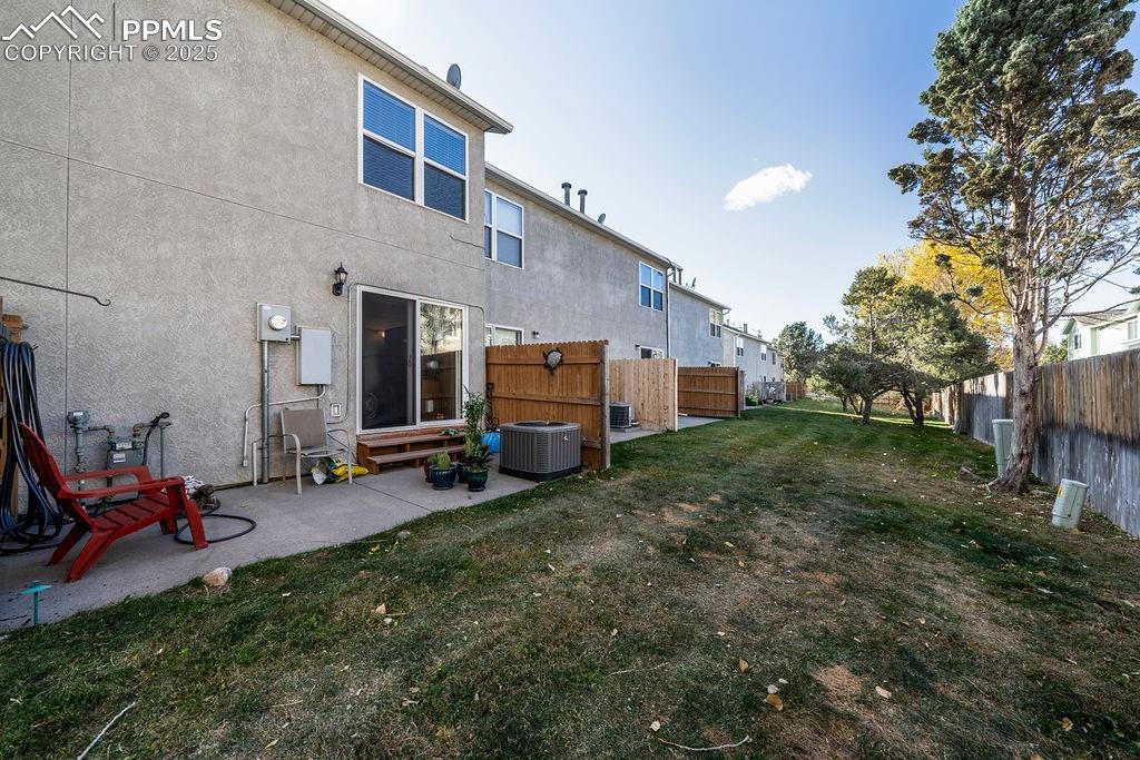 Image 36 of 37: Backyard area with concrete patio and green space with mature trees.