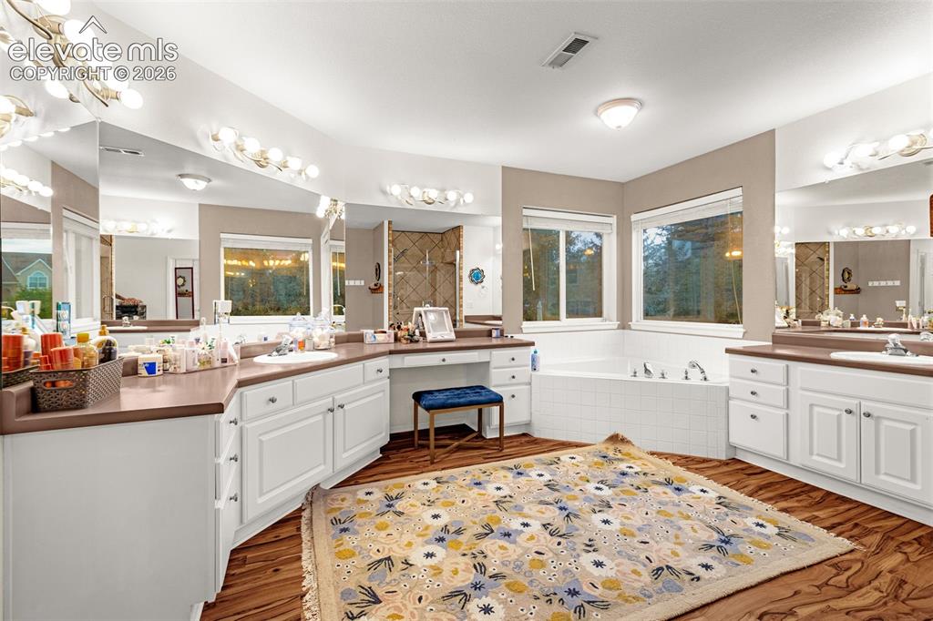 Image 20 of 50: Dual vanity with white cabinetry, built-in makeup desk, large soaking tub,