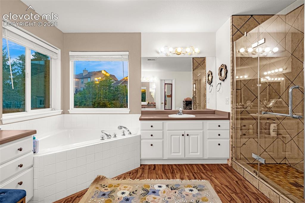 Image 22 of 50: Wood-finish flooring with a white built-in tub, white vanity with a single 