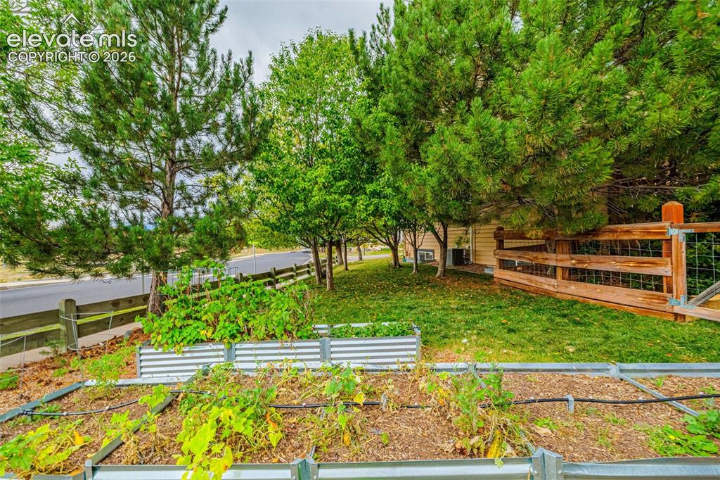 Image 39 of 50: Landscaped yard featuring raised garden beds, mature trees, and a wooden pe