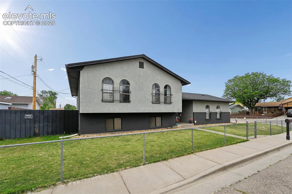 Image 17 of 20: Split-level residence featuring a light gray upper exterior with arched win