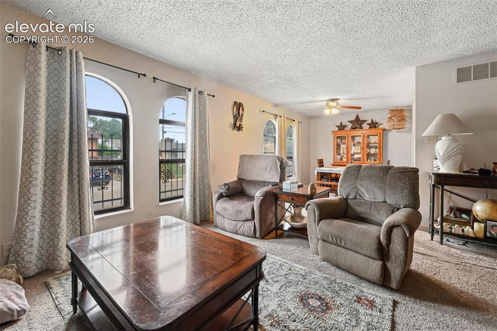 Image 2 of 20: Living area featuring arched windows with security grates, textured ceiling