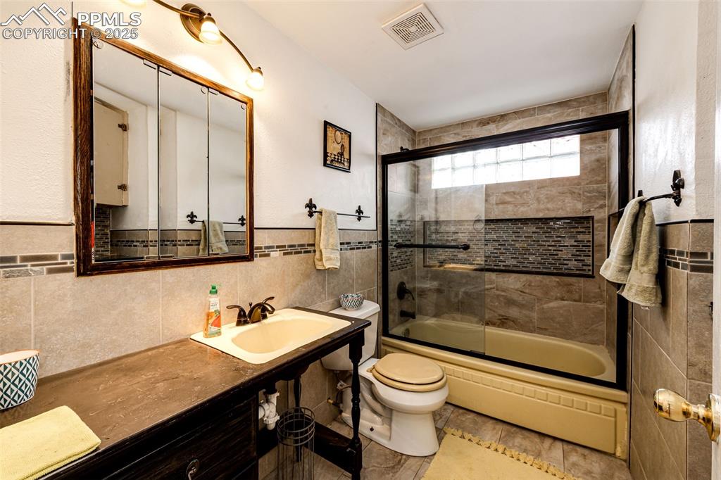 Image 17 of 34: Bathroom with combined bath / shower with glass door, toilet, wainscoting,