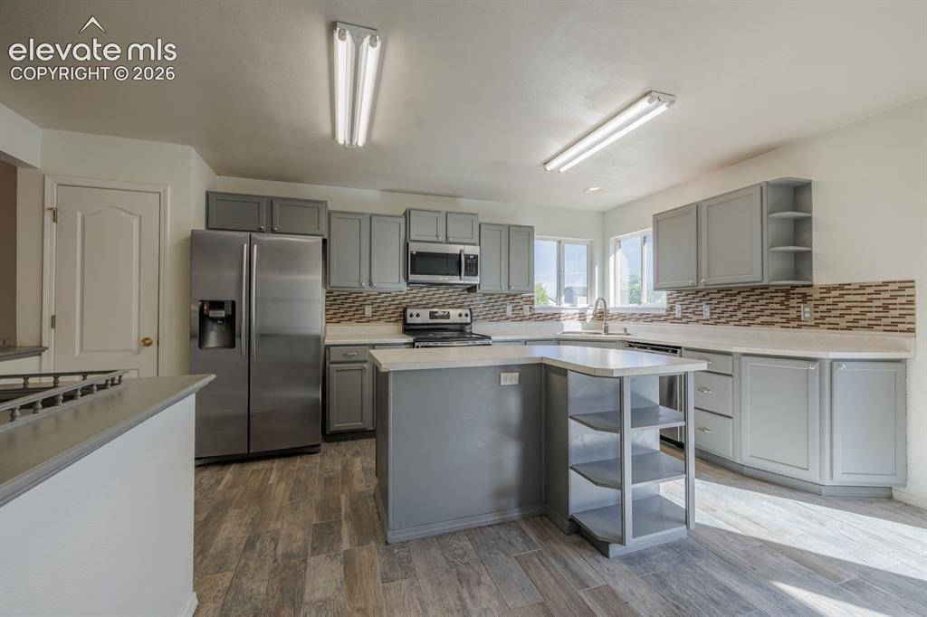 Image 13 of 36: Gray cabinetry, stainless steel appliances, wood-finish flooring, white cou