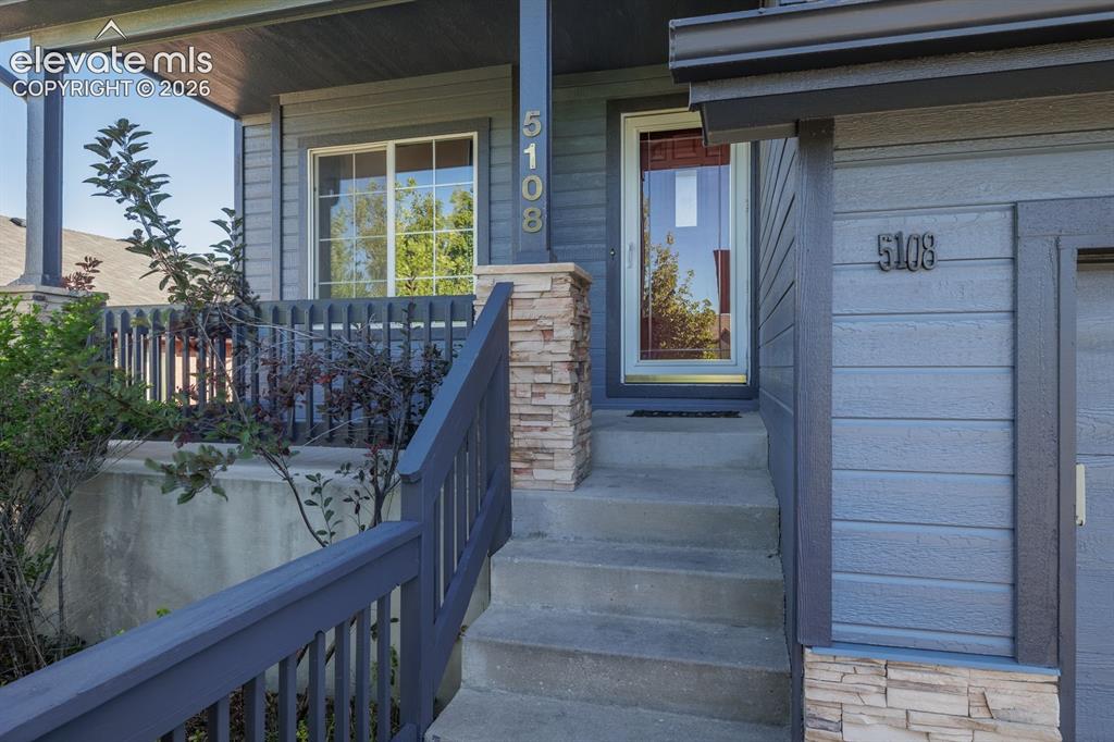Image 2 of 36: Covered front porch with stacked stone accents and concrete steps