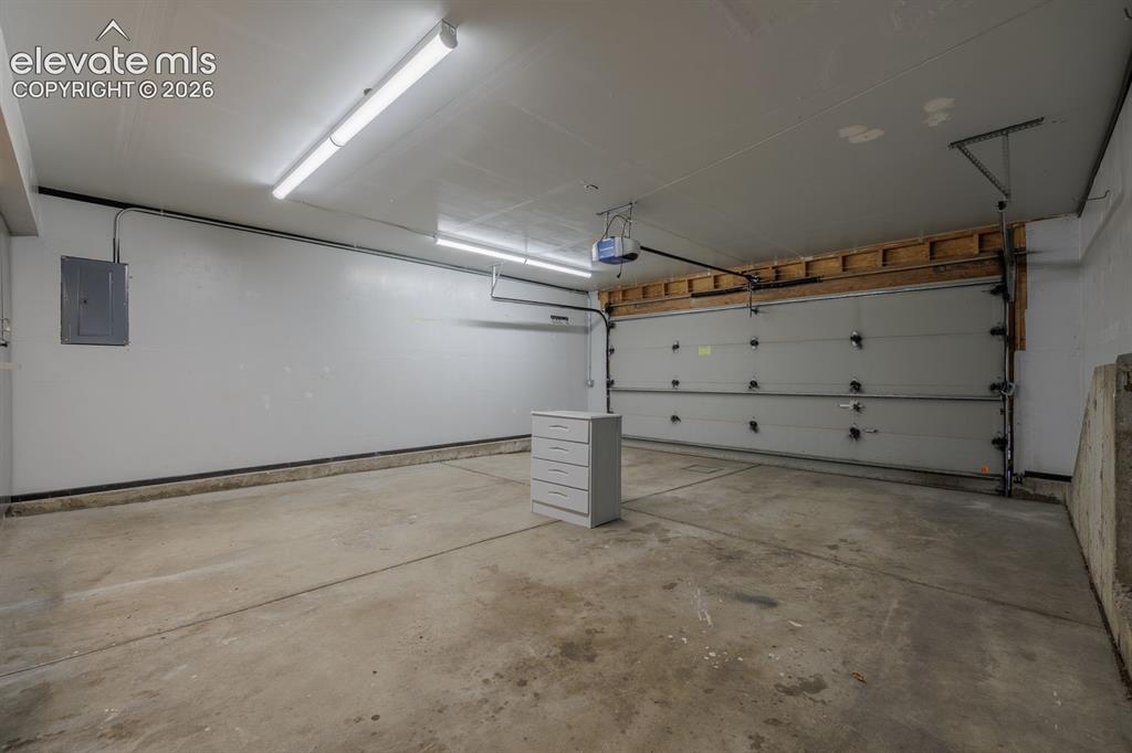 Image 28 of 36: Spacious garage featuring a concrete floor, overhead lighting, and an autom