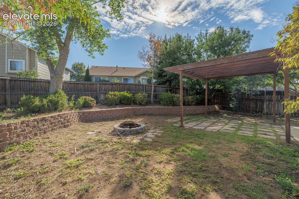 Image 30 of 36: Backyard featuring a wood pergola over a paver patio, a built-in fire pit,