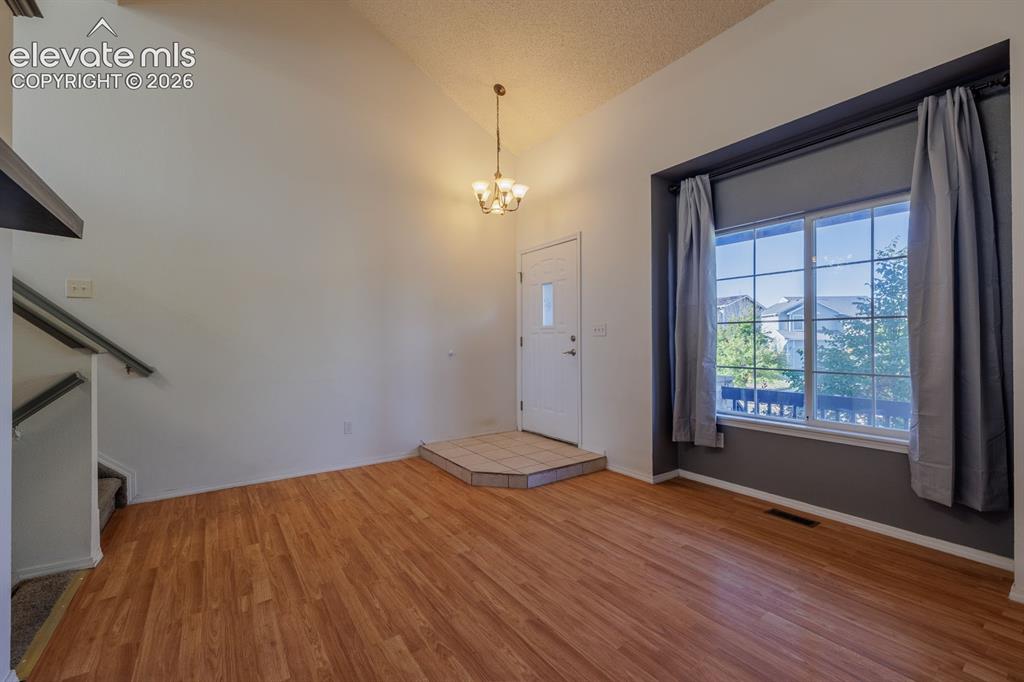 Image 6 of 36: Vaulted ceiling with an attached chandelier, wood-finish flooring, and a mu