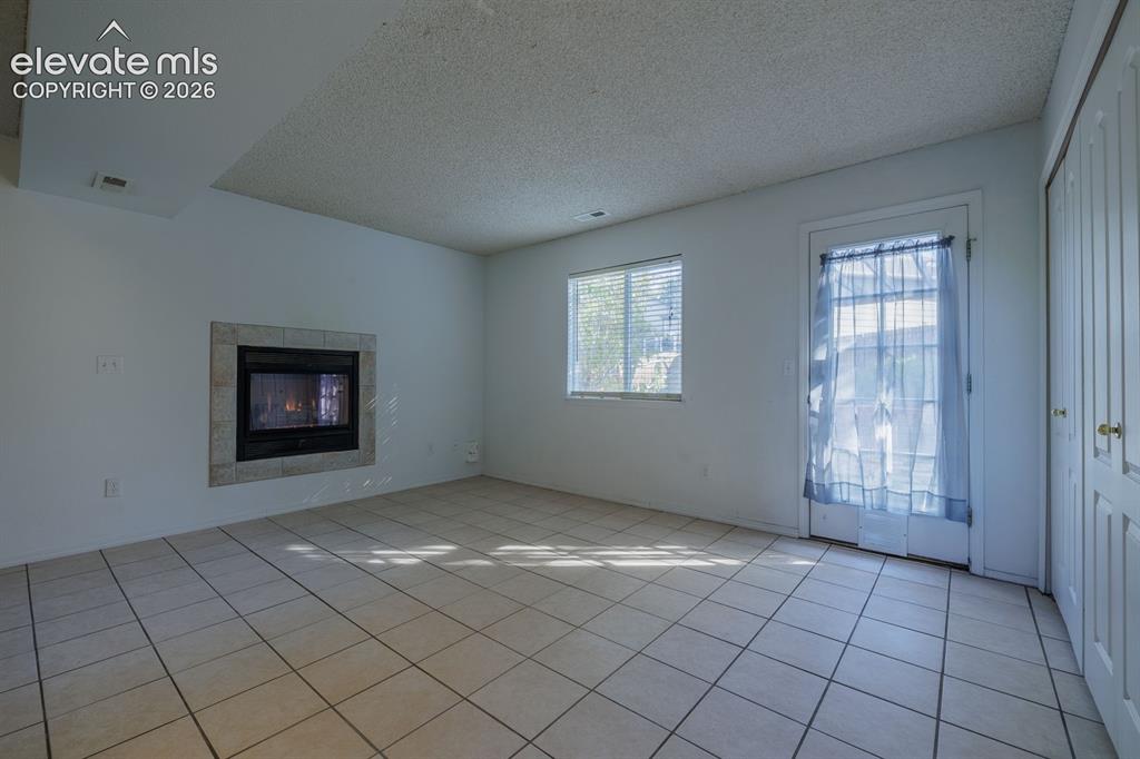 Image 7 of 36: Fireplace with stone surround, tile flooring, window with blinds, and white