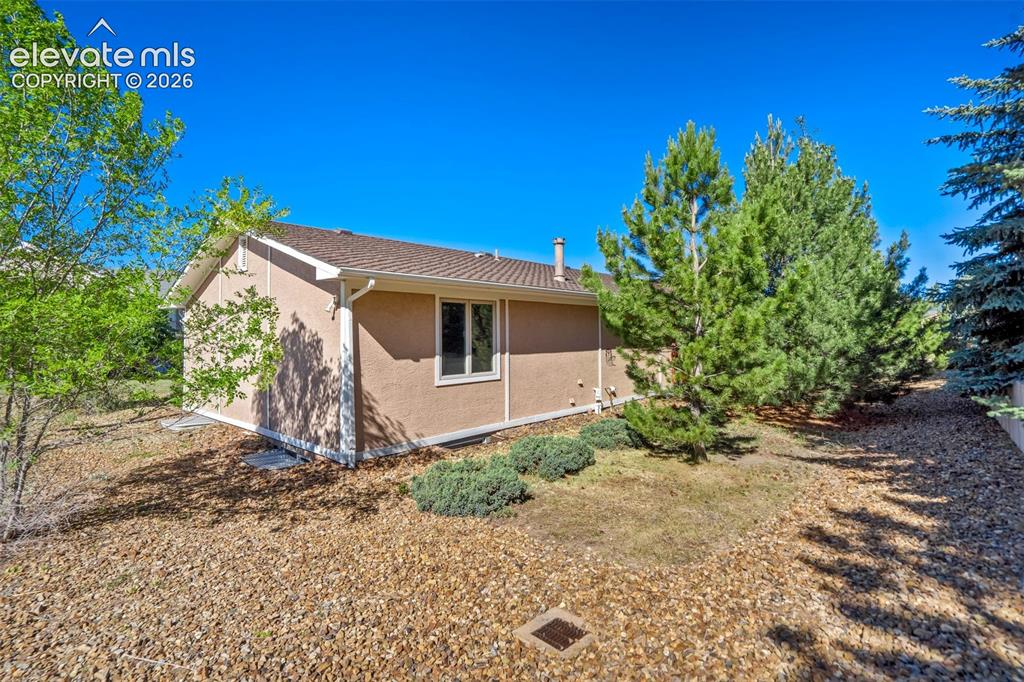 Image 40 of 45: Stucco exterior with a pitched shingle roof, framed by mature evergreens an