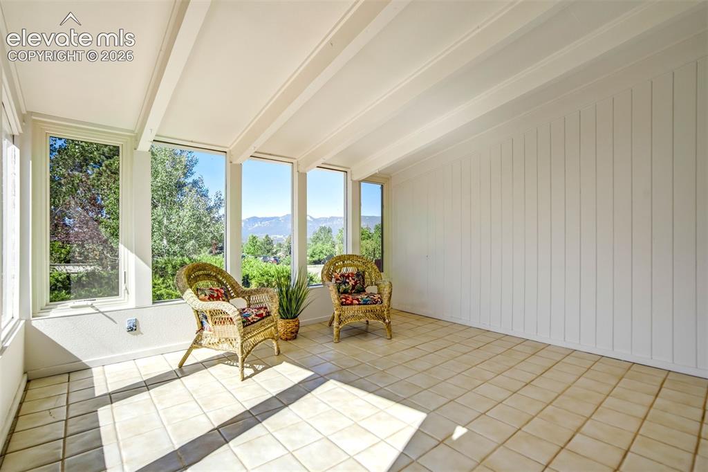Image 6 of 45: Sunroom featuring expansive windows, tile flooring, an exposed beam ceiling