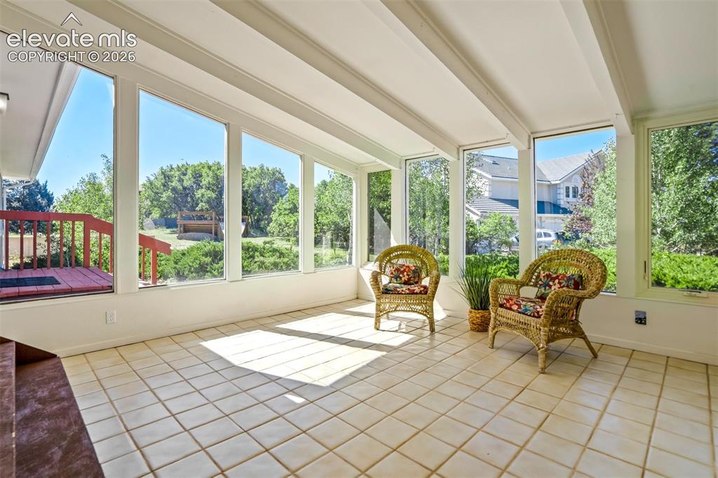 Image 7 of 45: Bright sunroom featuring a tiled floor, expansive windows, exposed ceiling