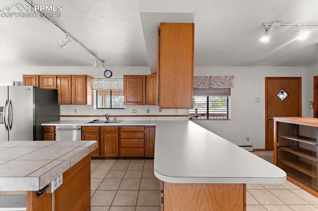 Image 12 of 44: Kitchen featuring track lighting, light tile patterned flooring, brown cabi