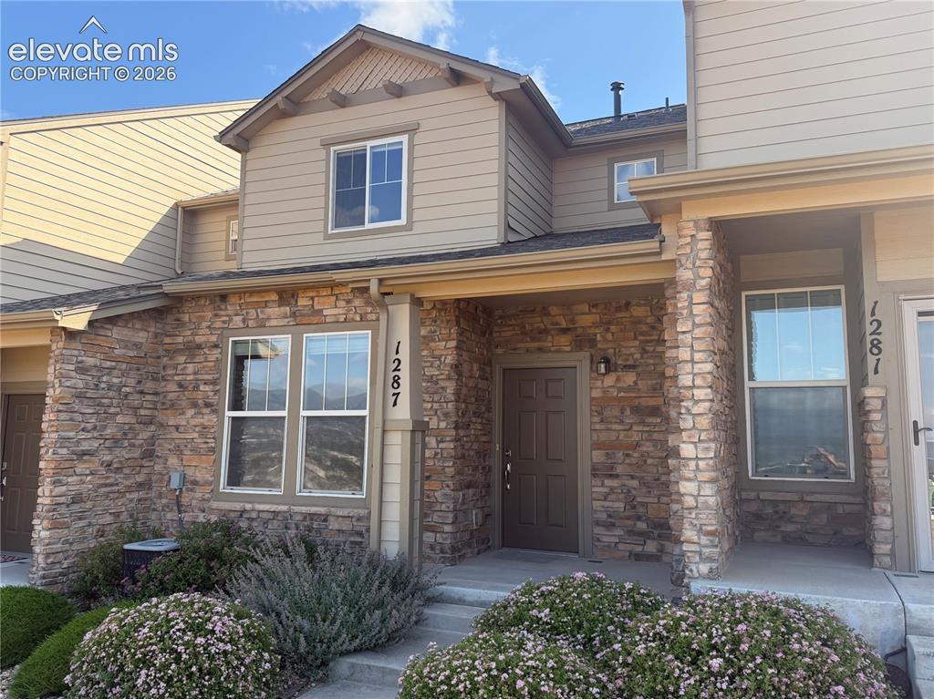 Caption: Stone veneer facade with siding accents, featuring a covered entryway, paneled front door, and visib