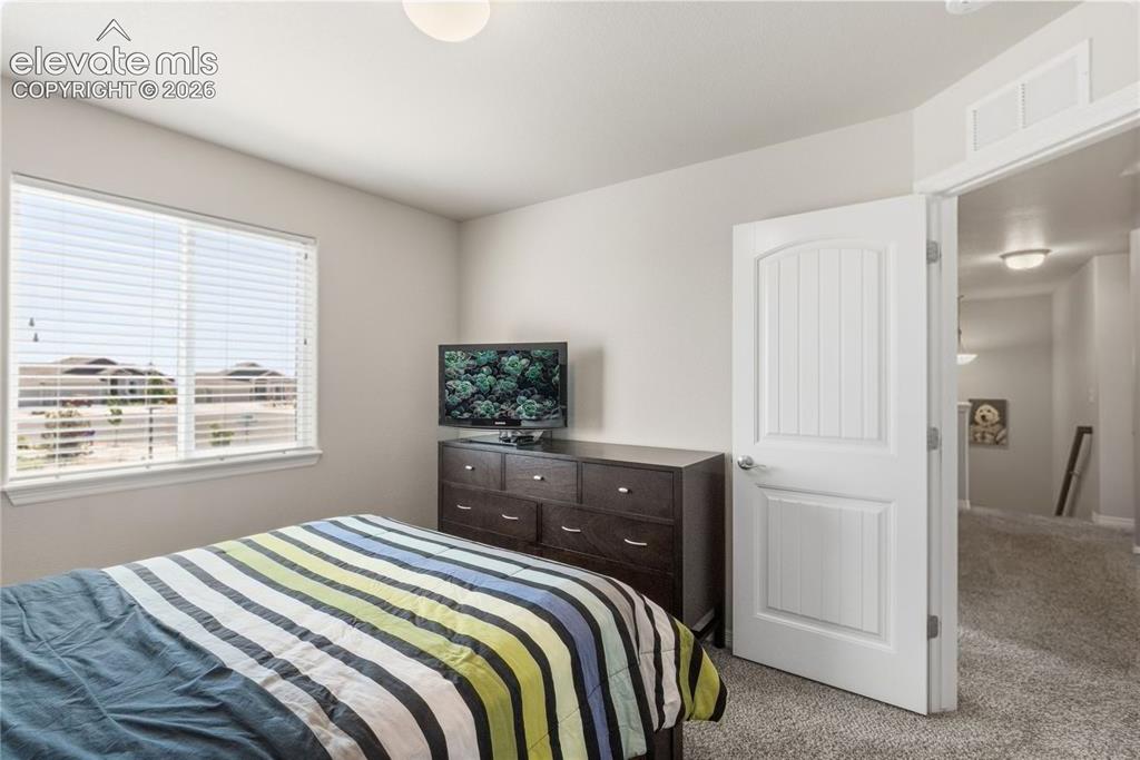 Image 21 of 50: Bright bedroom featuring a large window with blinds, light gray walls, and