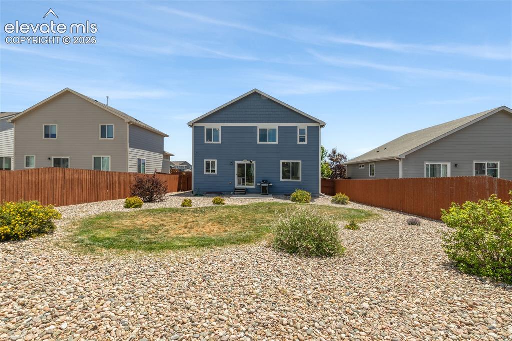 Image 36 of 50: Fenced backyard featuring a gravel landscape, central lawn, and surrounding