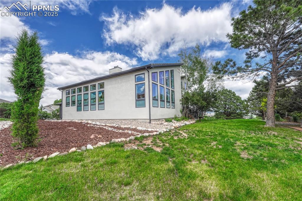Image 23 of 47: View of property exterior featuring stucco siding, a lawn, and a chimney