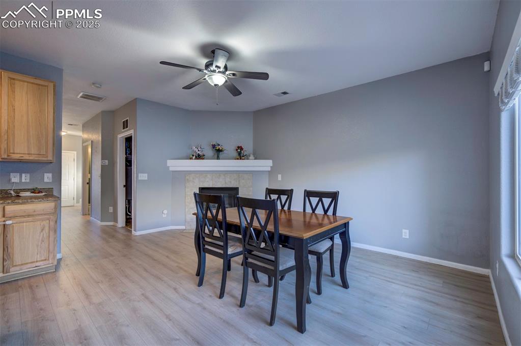 Image 13 of 43: Dining area with ceiling fan, light wood finished floors, and a tiled firep