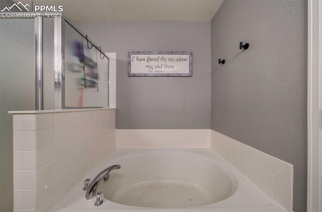 Image 35 of 43: Bathroom featuring a bath, a stall shower, a textured ceiling, and a textur