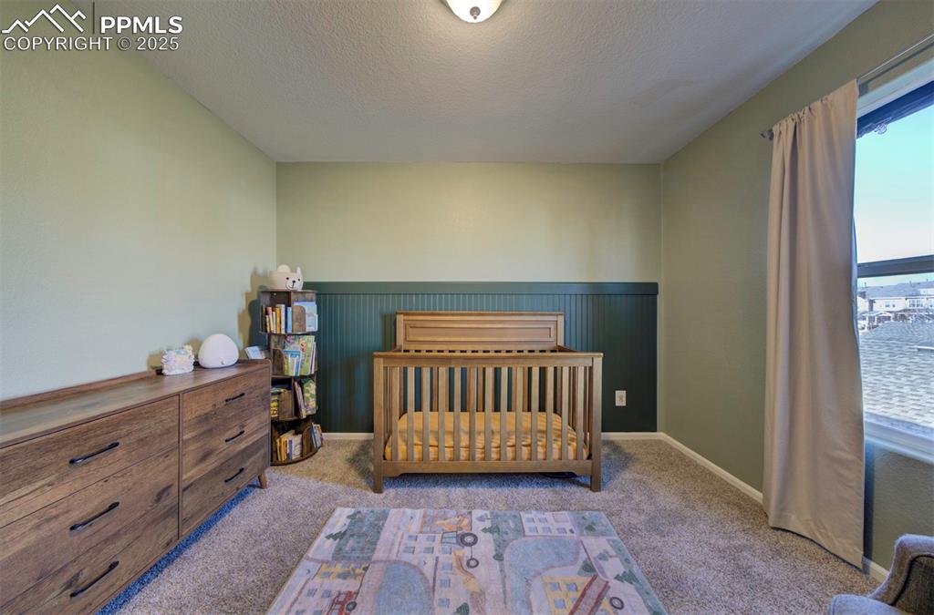 Image 40 of 43: Carpeted bedroom with a nursery area, a textured ceiling, and wainscoting
