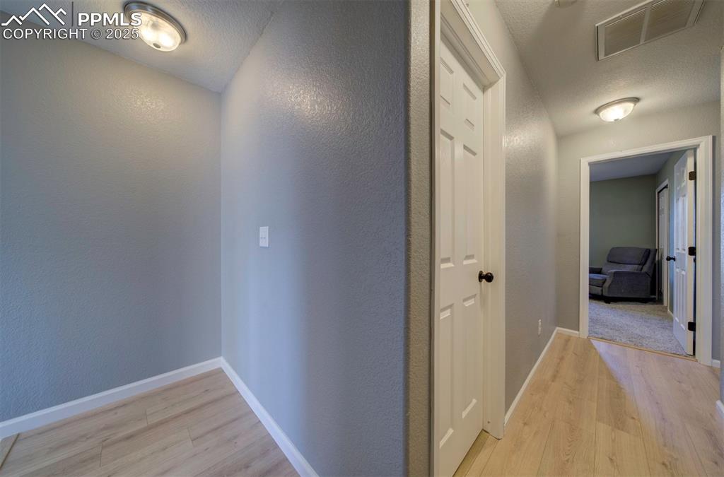 Image 41 of 43: Corridor with light wood-style flooring, a textured wall, and a textured ce