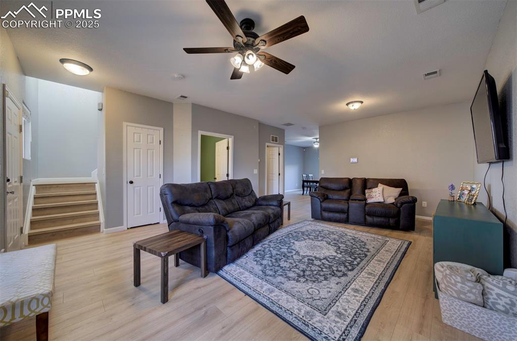 Image 8 of 43: Living room featuring a ceiling fan, stairway, and light wood-type flooring
