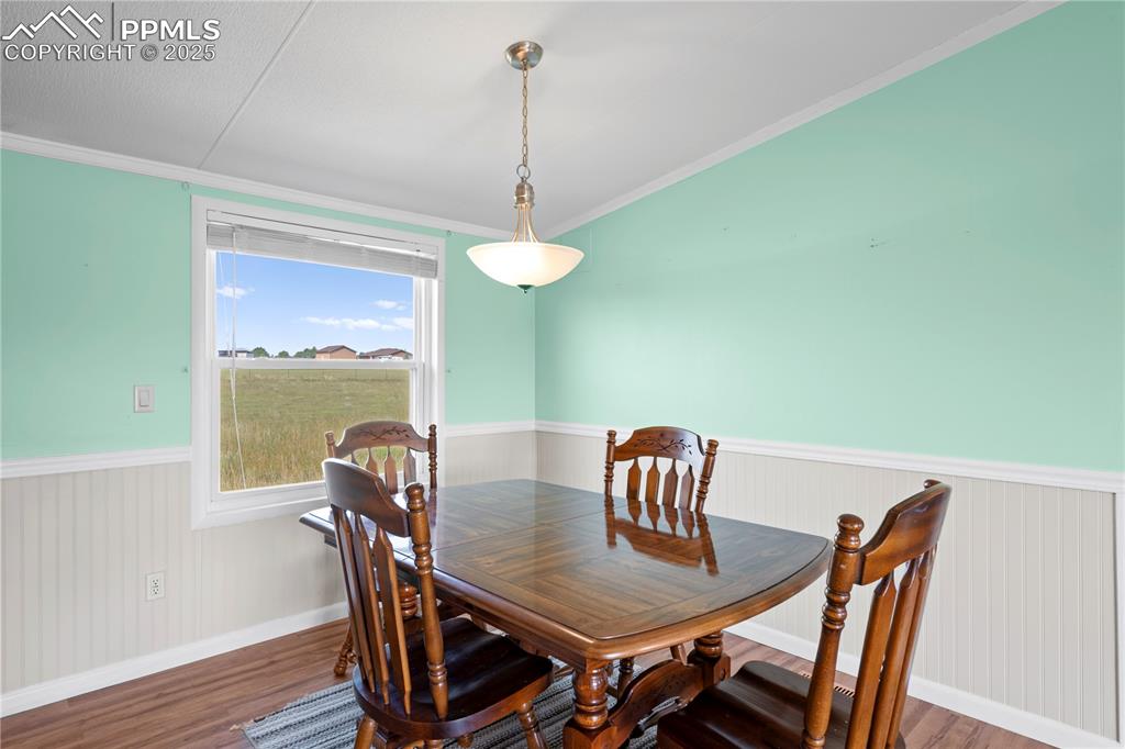 Image 10 of 29: Dining area with a wainscoted wall, dark wood-style floors, and crown moldi