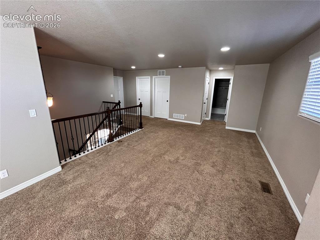 Image 12 of 24: Expansive carpeted area featuring a staircase with black wrought iron spind
