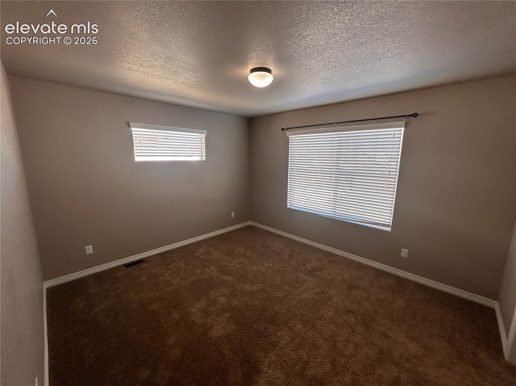 Image 13 of 24: Carpeted room with two windows, painted in a neutral tone, featuring white