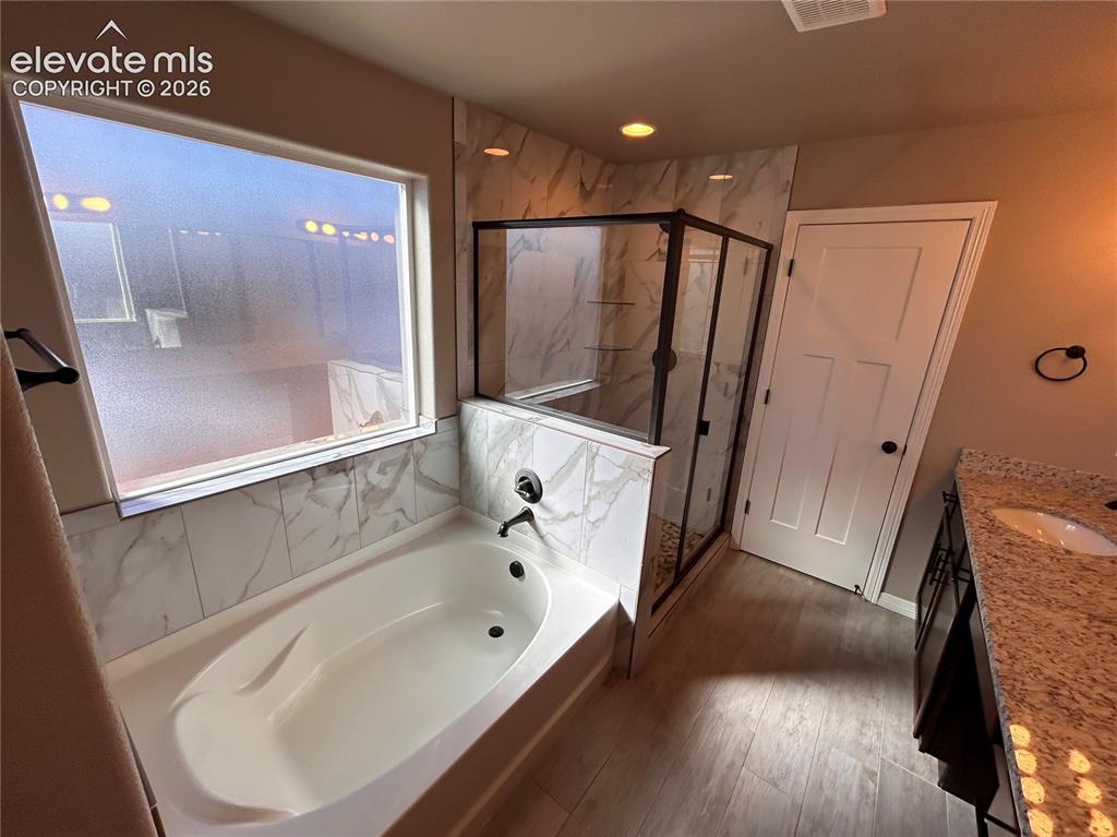 Image 23 of 24: Bathroom featuring a soaking tub, glass-enclosed shower, wood-finish floori
