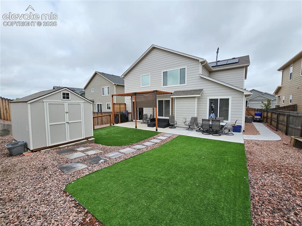 Image 24 of 24: Rear exterior featuring a concrete patio with pergola, artificial turf, roc