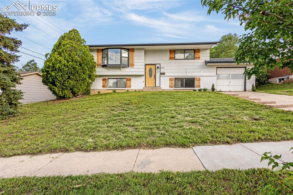 Caption: Bi-level home featuring an attached garage, driveway, a front lawn, and brick siding