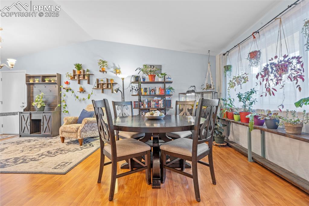 Image 24 of 50: Dining area featuring wood finished floors, vaulted ceiling, and a chandeli