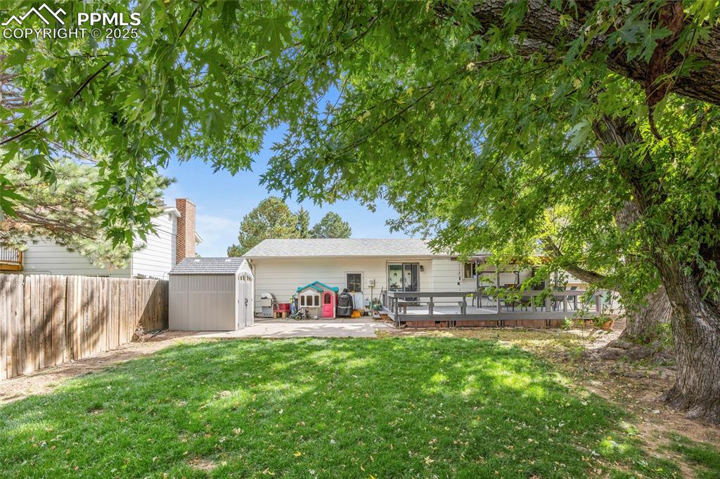 Image 38 of 50: Back of house with a storage shed, a wooden deck, a fenced backyard, and a