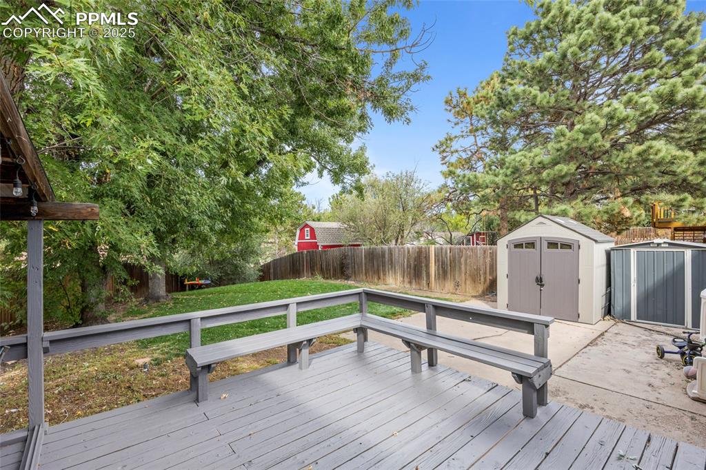 Image 42 of 50: Wooden deck with a storage unit and a fenced backyard